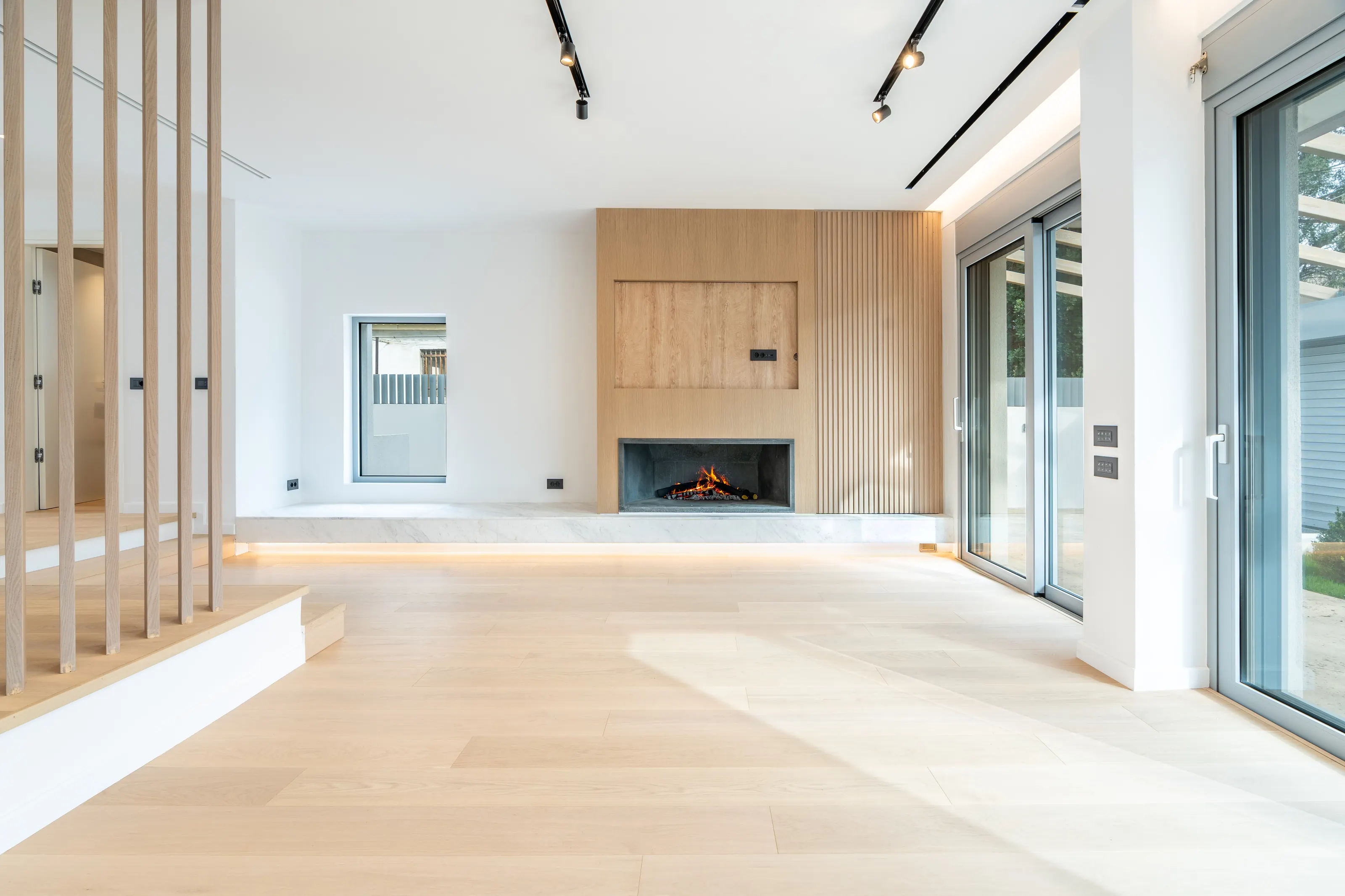 Bright living room with an oak-panelled fireplace wall, track lighting and full-height glass doors
