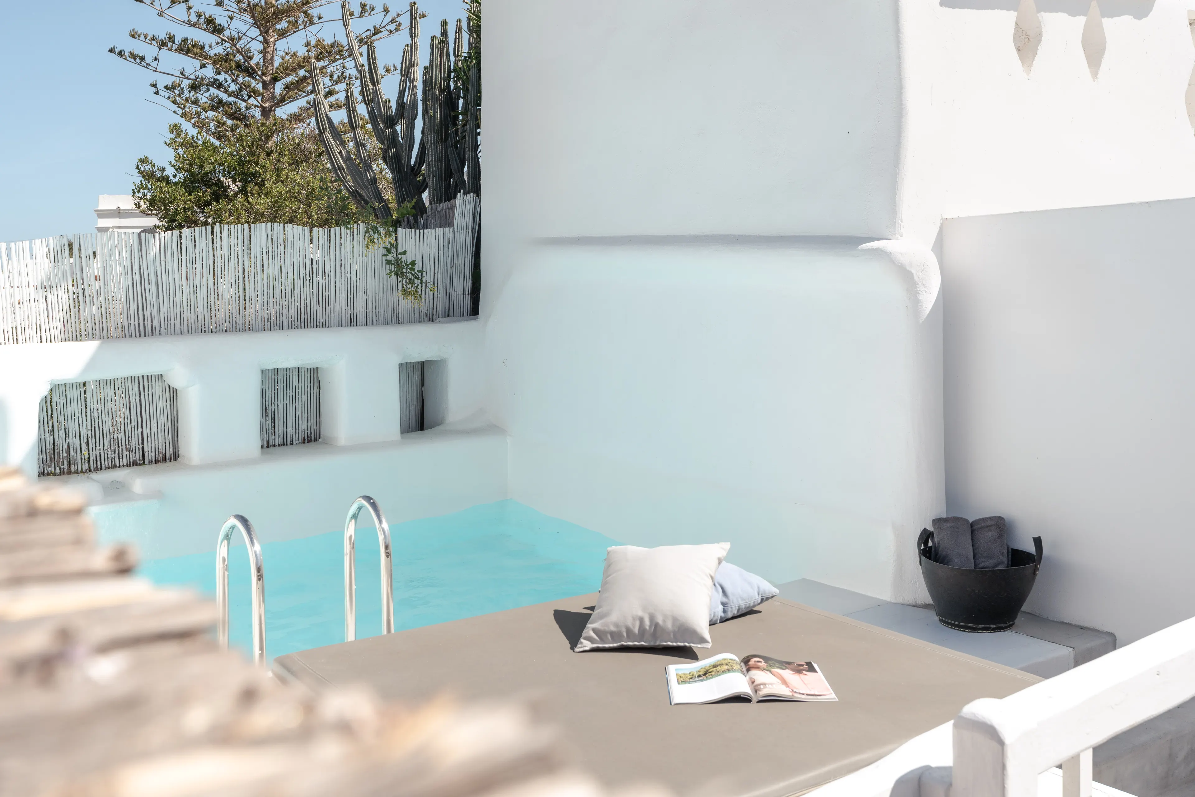 Private whitewashed terrace with a turquoise plunge pool, a daybed, cushions and an open magazine